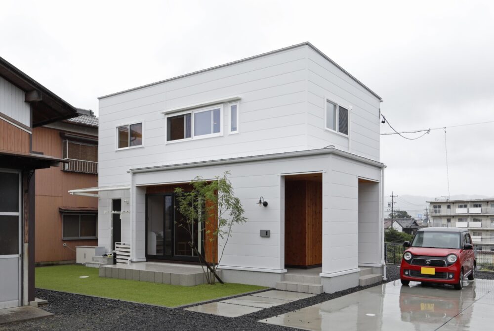 白い外壁に木目がアクセントの外観と芝生の庭