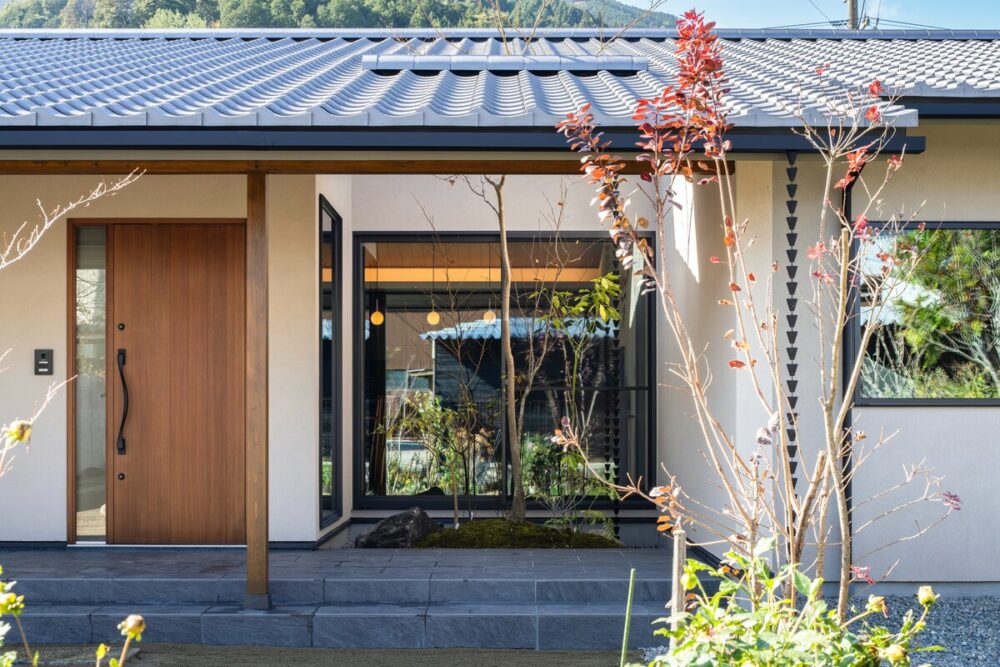 白い外壁と瓦屋根の平屋の玄関アプローチと豊かな植栽