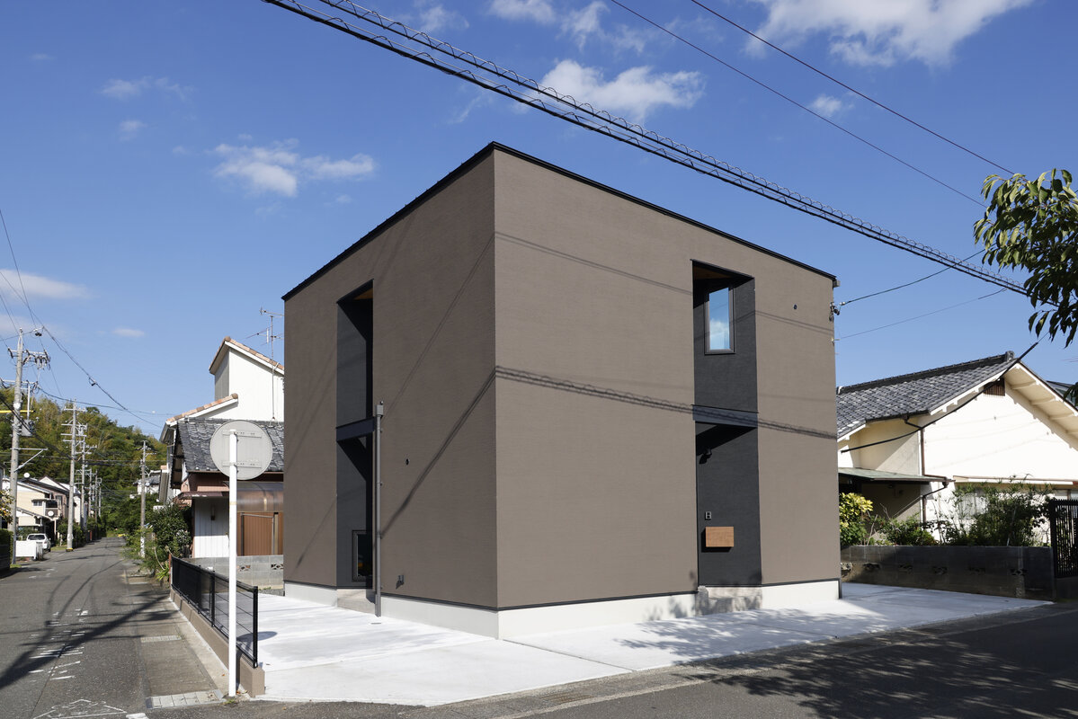 ブラウンと黒の外壁の四角い二階建て住宅と駐車スペース